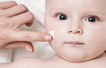 De hand van een volwassene brengt crème op het gezicht van een baby aan.