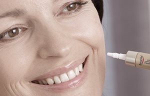 Een vrouw smeert Eucerin-product op haar linkerwang.