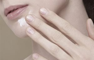 Een vrouw smeert crème op haar kin.