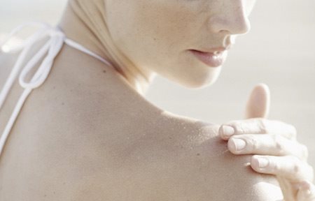 Een vrouw brengt crème op haar rechterschouder aan.